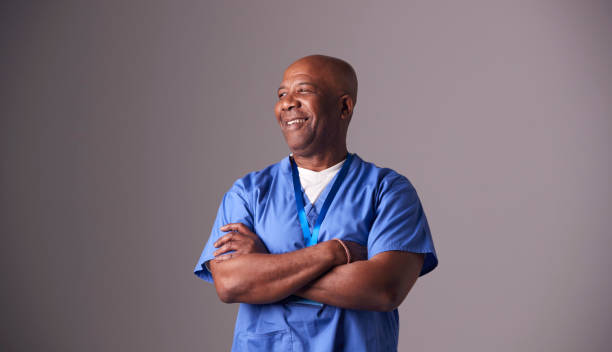 studio portrait of male nurse wearing scrubs standing against grey background - male nurse black nurse doctor imagens e fotografias de stock