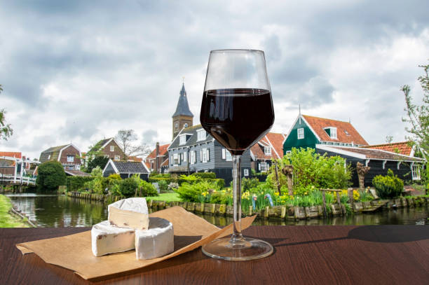 copa de vino tinto y brie chhese con vistas al canal, puente y casas de pesca tradicionales de madera en el pueblo de marken, países bajos. - waterland fotografías e imágenes de stock