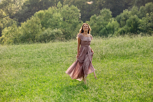 Teenage girl is hiking in the Cotswolds, Worcestershire, United Kingdom. She is standing on the beautiful meadow on top of the hill and looking at the view\nSunny and cloudy, summer day.\nShot with Canon R5