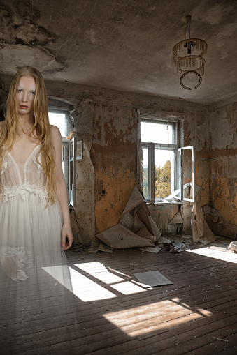 Ghost of a girl in a room of an old abandoned house with torn wallpaper and broken windows