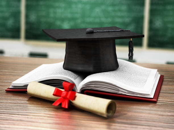 istock Mortarboard, open book and diploma standing on classroom desk 1287399265