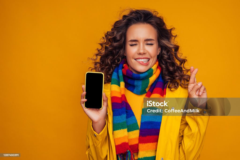 Beautiful girl with smart phone crossing her fingers and wishing for good luck Luck Stock Photo