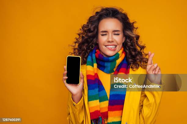 Beautiful Girl With Smart Phone Crossing Her Fingers And Wishing For Good Luck Stock Photo - Download Image Now