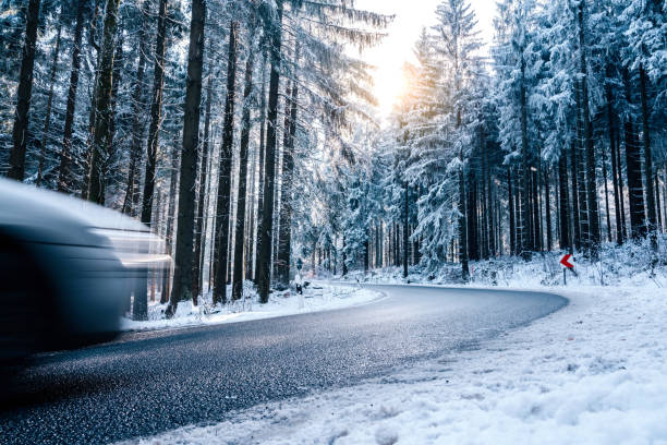 A snow-covered and icy road in a forest in south-west Poland. The rays of the setting sun between the trees.