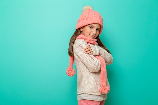 Child wearing warm winter knitwear isolated on mint colored background with copy space