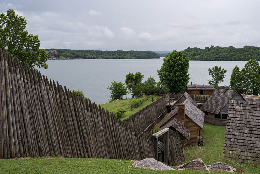 A recreation of Fort Loudon in TN showing some of the old cabins  and fence with a lake in the distance.