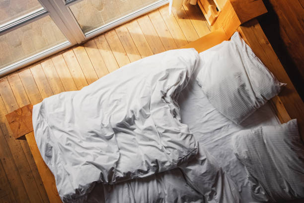 istock Bed with white bedding near the window in wooden rustic house 1287404887
