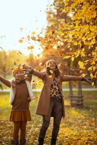 istock smiling modern mother and daughter throws up autumn leaves 1287406396