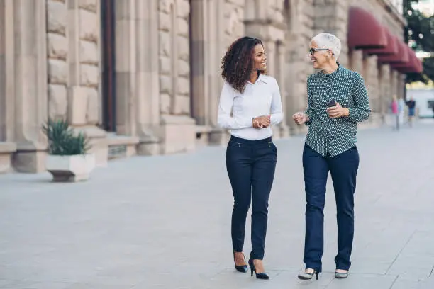 Two businesswomen walking together and talking outdoors in the city