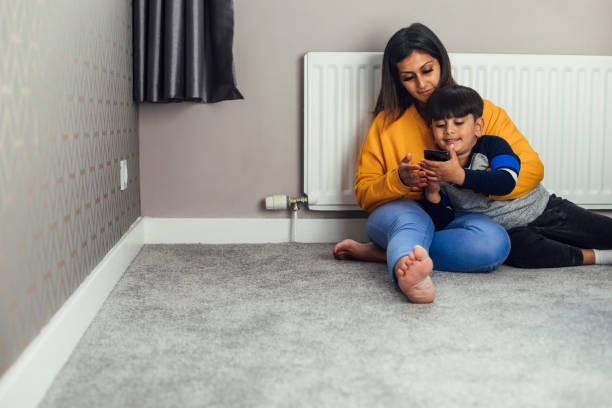 Controlling the Heating With the Mobile Phone A shot of a mid adult woman and her little boy wearing casual clothing. They are sitting on the floor by a radiator and are controlling the heating with a home control centre on a mobile phone. pakistani ethnicity stock pictures, royalty-free photos & images