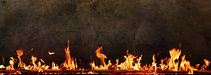 Fire with lots of flames in front of dark concrete wall. Horizontal background with space for text.