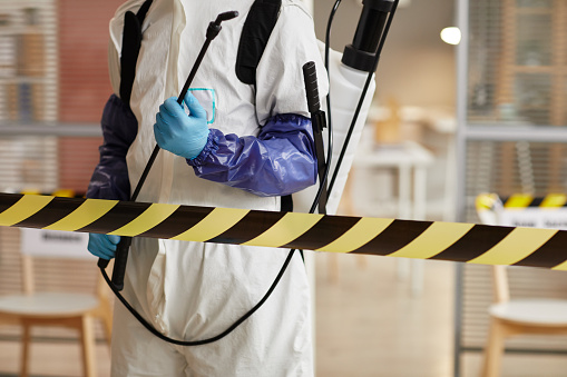 Cropped portrait of unrecognizable disinfection worker wearing full protective gear standing behind danger line while sanitizing office, copy space