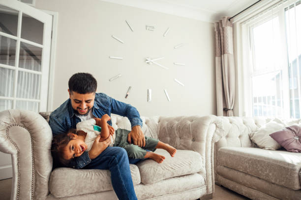 Father and Son Playing on Sofa in Living Room A shot of a mid adult male and his young toddler son wearing casual clothing. They are playing on a sofa in their living room. pakistani ethnicity stock pictures, royalty-free photos & images