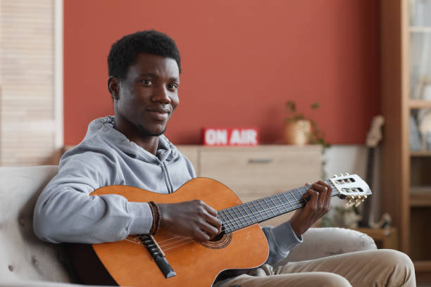 istock Smiling African-American Man Playing Guitar at Home 1287419227