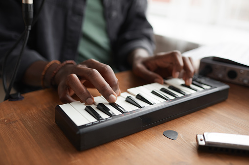 Close up of unrecognizable African-American man playing music on keyboard while composing at home, copy space
