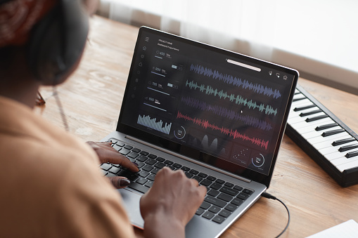 Close up of female African-American musician using laptop with sound editing software while composing music at home, copy space