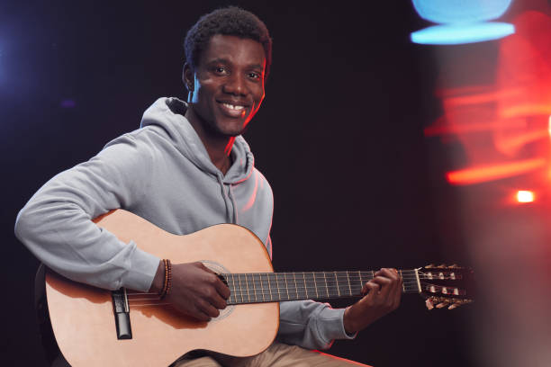istock Smiling African-American Man Playing Guitar on Stage 1287419327