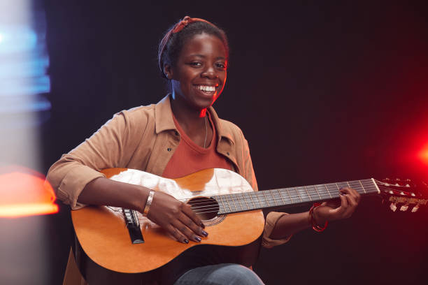 istock Smiling African-American Woman Playing Guitar on Stage 1287419330