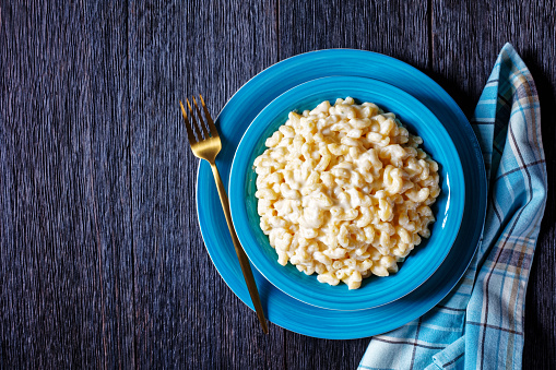 classic mac and cheese in a blue bowl with golden fork and napkin on a wooden table, horizontal view from above, flat lay, free space