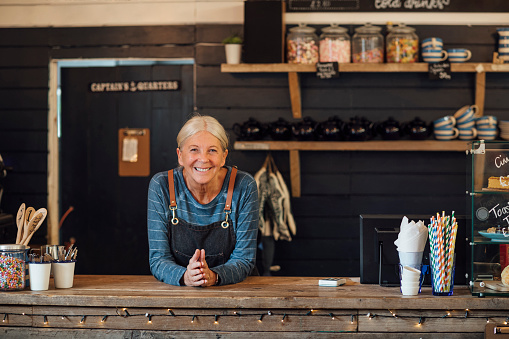 A shot of a senior female standing behind the counter in a coffee shop ready to serve customers.