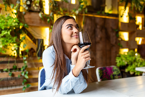 Beautiful woman tasting wine while sitting in restaurant. Image of cute pretty young woman sitting in cafe holding glass and drinking wine. portrait of a beautiful wine tasting tourist woman.