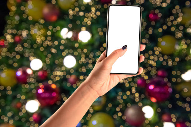istock Close up hand holding phone isolated on white background with Illuminated  blurred bokeh of  Christmas tree decoration with  hanging lights ball. 1287429118