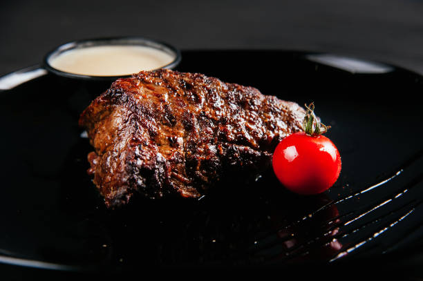 istock Close up grilled steak in dark plate with tomatoes and sauce 1287432237