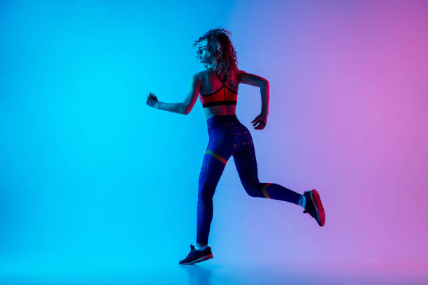 istock Young sportive woman running isolated on gradient pink-blue studio background in neon light. 1287432451