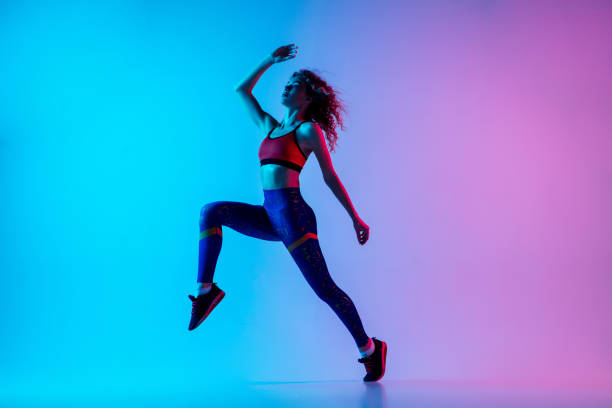 istock Young sportive woman running isolated on gradient pink-blue studio background in neon light. 1287432454