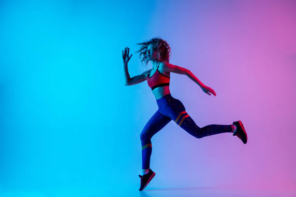 istock Young sportive woman running isolated on gradient pink-blue studio background in neon light. 1287432459