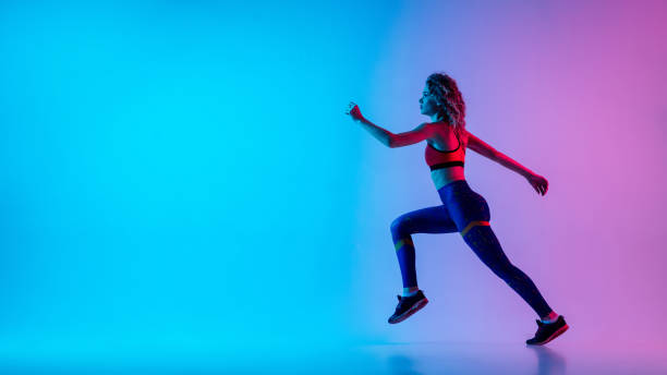 istock Young sportive woman running isolated on gradient pink-blue studio background in neon light. 1287432462