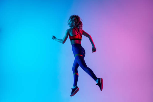 istock Young sportive woman running isolated on gradient pink-blue studio background in neon light. 1287432463