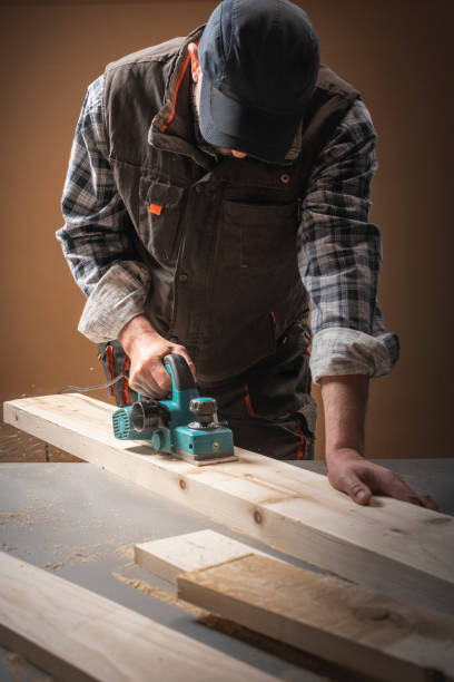 istock Worker planing a table top of wood with a electric plane. 1287435885