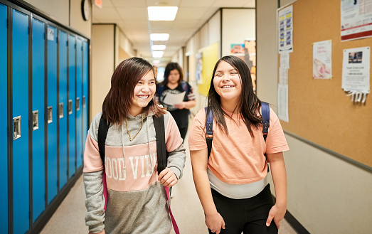 Two school girls walking down the school corridor and smiling in front of lockers