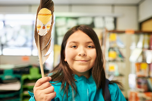 Close-up of a girl in school classroom showing a bird feather with a painting