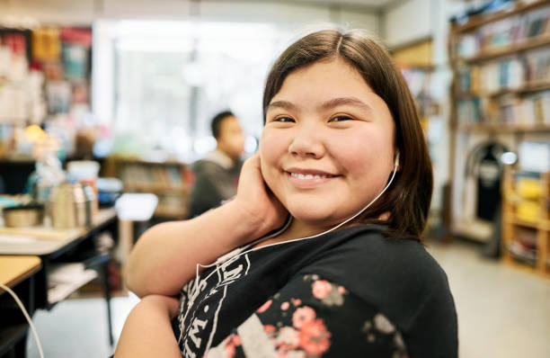 She's a happy pupil Close-up of a happy girl sitting on school classroom wearing earphones looking at camera and smiling high school student photos stock pictures, royalty-free photos & images