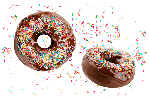 Many donuts fly covered with chocolate frosting and decorated with colorful sprinkles isolated on a white background. Funny and delicious doughnuts