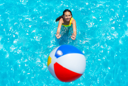 Girl stand in swimming pool throw inflatable ball view from above