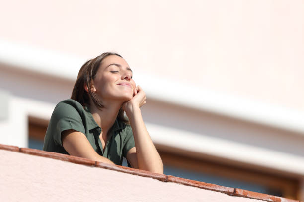 mujer feliz respirando aire fresco desde el balcón en el apartamento - aliento fotografías e imágenes de stock