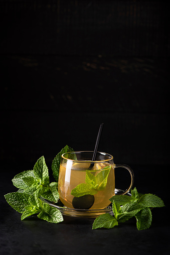 herbal tea with mint and lemon in a glass mug on black bsckground