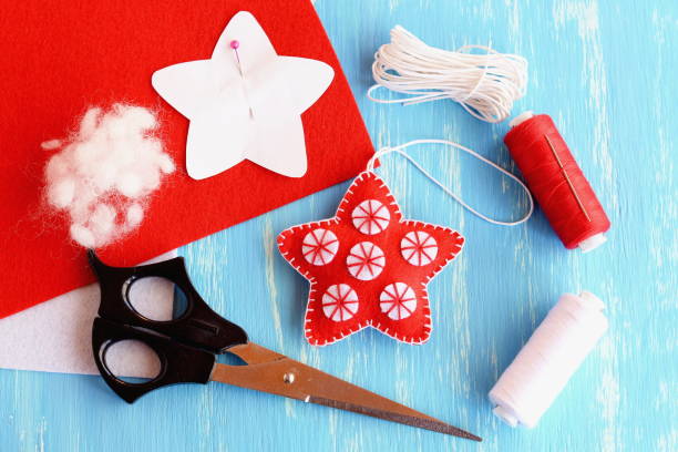 Felt Christmas background. December activities for kids art projects. Children sewing training. Christmas step by step craft diy tutorial. Red Christmas gifts. Sewing table background. Kids Christmas diy. Making decorations diy. Holiday workshop. Christmas ornaments diy. Handicrafts background. New year Christmas background. Sewing tools accessories, tailor workplace. Children craft making fieltro niños navidad estrella decoración diy, patrón de papel anclado a la hoja de fieltro rojo, tijeras, hilo, aguja, cordón sobre fondo de madera azul. vacaciones de invierno navidad fondo vista superior. proyecto de artesanía de invierno para niñ