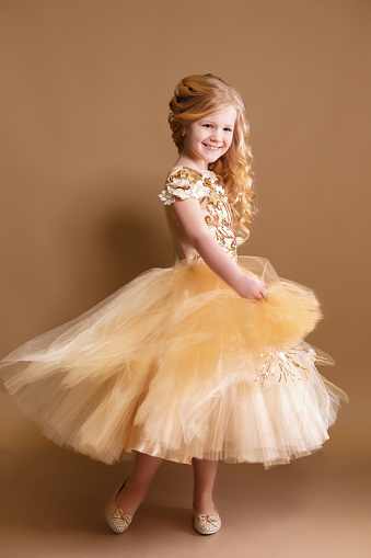 little girl like a doll with curly golden hair in nice gold dress in studio shoot