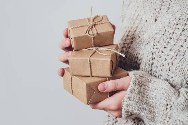 cadeaux dans les mains des femmes, gros plan. concept cadeau monochrome et minimaliste. une fille dans un chandail retient des boîtes-cadeaux faites de papier kraft, attachées avec une corde. fond de surprise, carte de voeux - wrapped package string box photos et images de collection