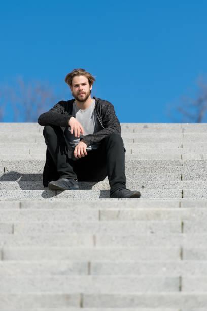 istock thoughtful young man sitting on steps against blue sky background 1287450029