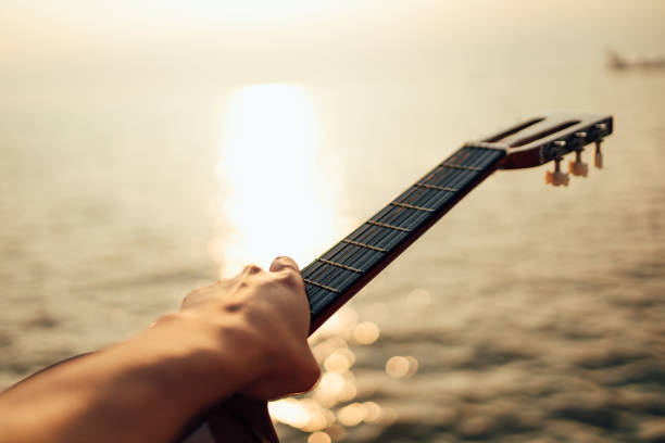 istock man playing guitar on sunset sea beach. 1287452295