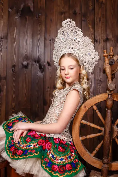 Russian girl in a folk russian dress on wooden background with spinning wheel