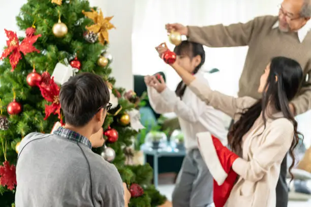 Multigenerational asian Family decorating a Christmas tree. Mom Dad daughter girl and grandfather decorate the Christmas tree prepare for season greeting of Merry Christmas and Happy Holidays.