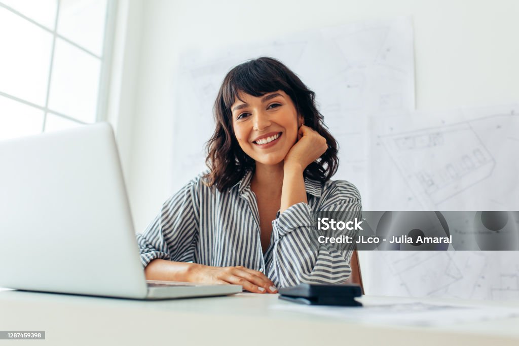 Usmívající se architektka sedící u svého kancelářského stolu - Bez autorských poplatků Pouze jedna žena - Pouze ženy Stock fotka