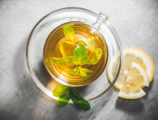 Glass cup of mint tea leaves with fresh slice lemon on gray table. Top view, above. Close up