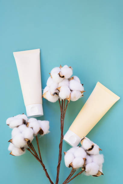 istock Vertical format photo with two beige tubes on blue background with soft cotton branches. 1287461085